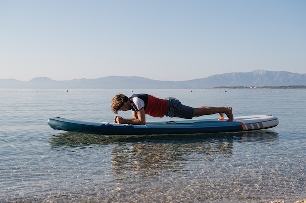 Junger Mann, der Planke auf sup Brett macht