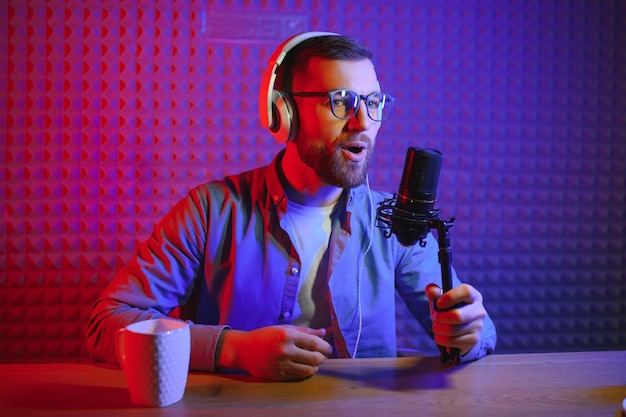 Junger Mann, der Podcasts mit Mikrofon in seinem kleinen Sendestudio aufnimmt oder streamt Inhaltsersteller