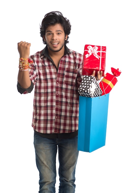 Junger Mann, der Rakhi auf seiner Hand mit Einkaufstüten und Geschenkbox anlässlich des Raksha Bandhan Festivals zeigt.