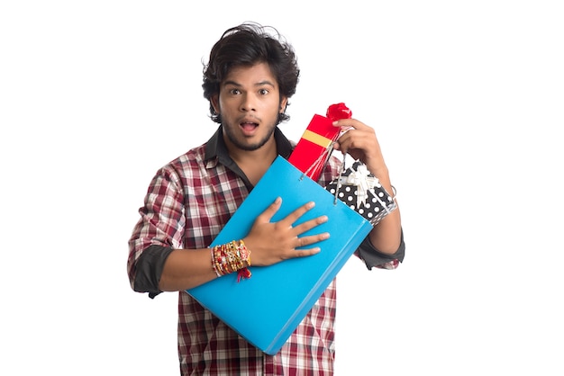 Junger Mann, der Rakhi auf seiner Hand mit Einkaufstüten und Geschenkbox anlässlich des Raksha Bandhan Festivals zeigt.
