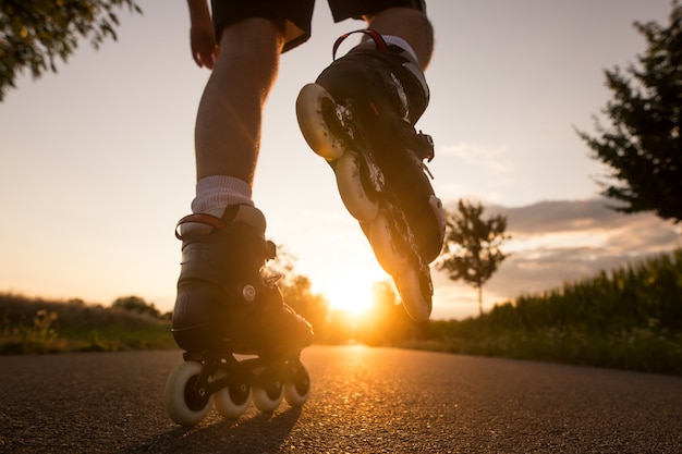 Junger Mann, der Rollschuhlaufen auf dem Radweg während des schönen Sommersonnenuntergangs genießt