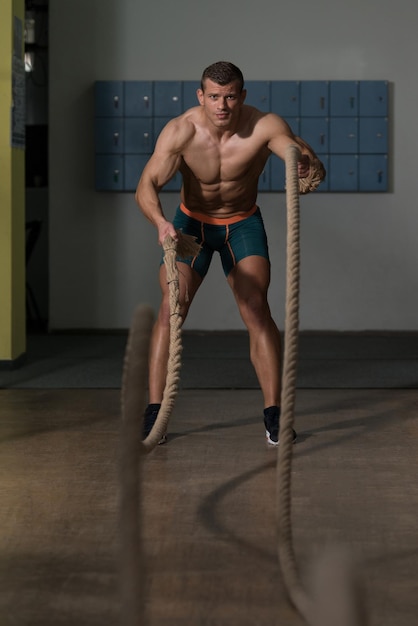 Junger Mann, der Seile an der Gymnastik-Trainingsübung kämpft