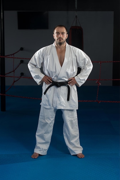 Junger Mann, der seine Karate-Bewegungen übt, weißer Kimono, schwarzer Gürtel