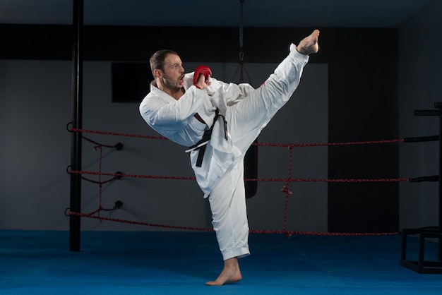 Junger Mann, der seine Karate-Bewegungen übt, weißer Kimono, schwarzer Gürtel