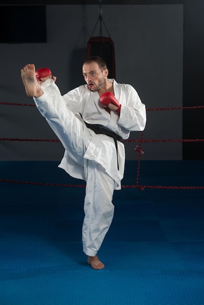 Junger Mann, der seine Karate-Bewegungen übt, weißer Kimono, schwarzer Gürtel