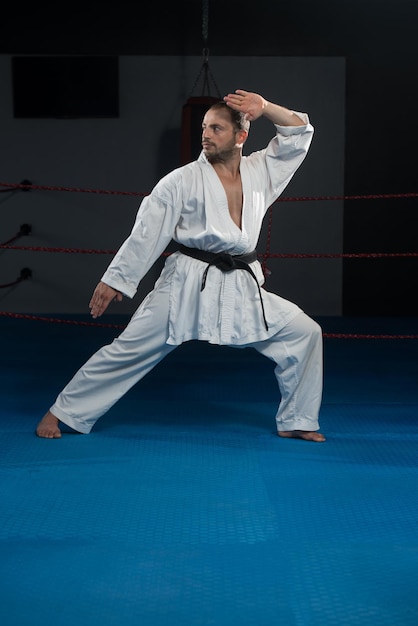 Junger Mann, der seine Karate-Bewegungen übt, weißer Kimono, schwarzer Gürtel