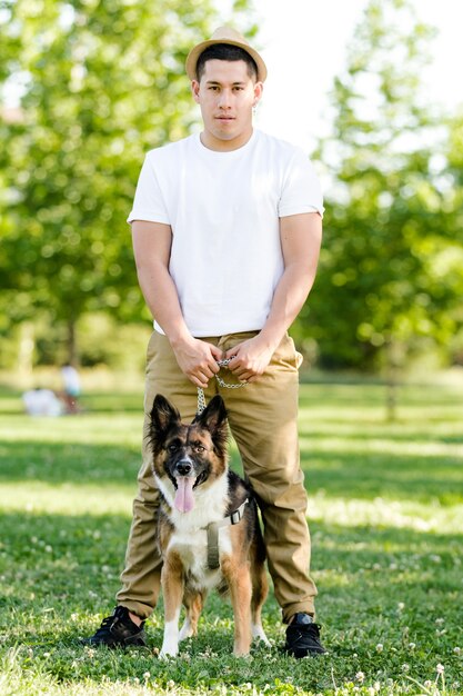 Junger Mann, der seinen Hund im Park geht. Lateinisches Modell posiert und schaut vor der Kamera