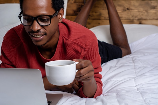 Junger Mann, der seinen Laptop im Bett verwendet