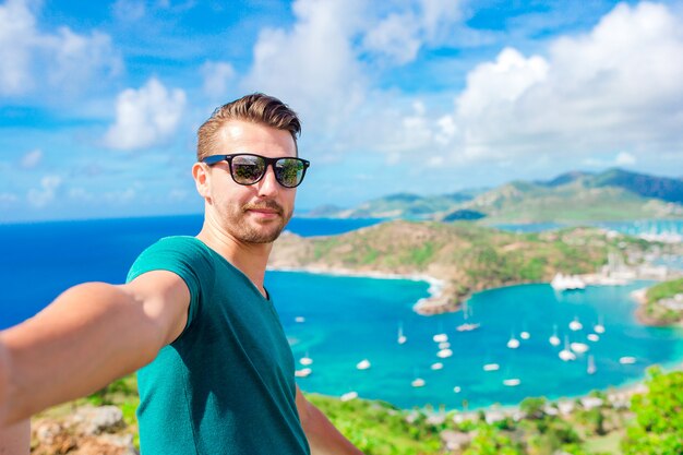 Junger Mann, der selfie mit Blick auf englischen Hafen von Shirley Heights, Antigua, Paradiesbucht in Tropeninsel im karibischen Meer nimmt