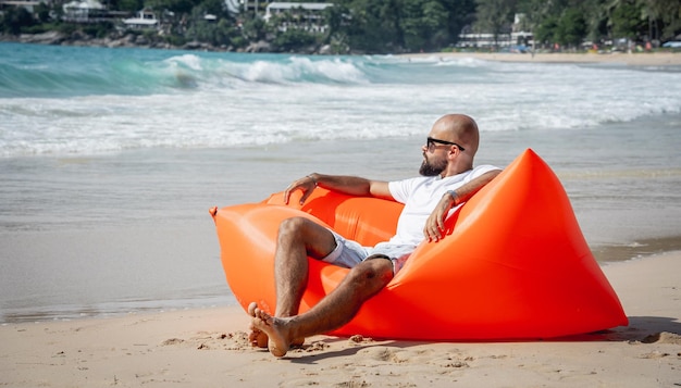 Junger Mann, der sich am Strand entspannt, während er auf einem aufblasbaren Sofa sitzt