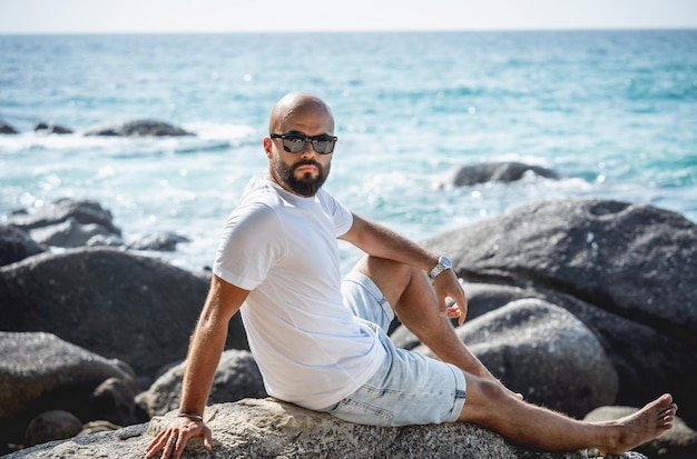 Junger Mann, der sich am Strand entspannt, während er auf einem Stein sitzt