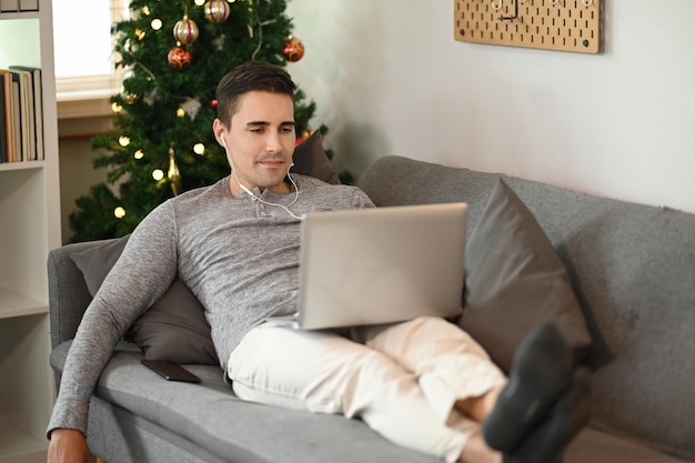 Junger Mann, der sich auf der Couch entspannt und zu Hause einen Laptop benutzt