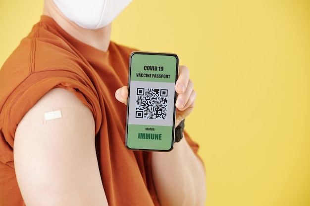 Junger Mann, der Smartphone mit QR-Code zeigt, nachdem er einen Impfstoff gegen Coronavirus erhalten hat