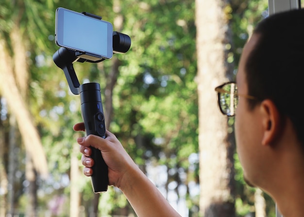 Junger Mann, der Stabilisator für Handy verwendet und den Wald filmt