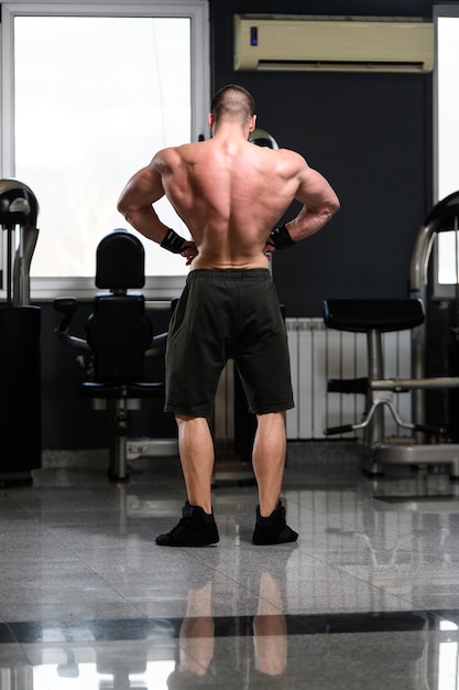 Junger mann, der stark in der turnhalle steht und muskeln muskulöser athletischer bodybuilder-eignungs-modell aufwirft, das nach übungen aufwirft