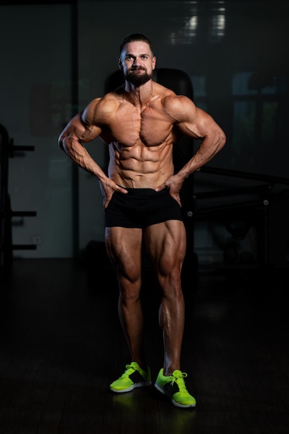 Junger Mann, der stark in der Turnhalle steht und Muskeln muskulöser athletischer Bodybuilder-Eignungs-Modell aufwirft, das nach Übungen aufwirft
