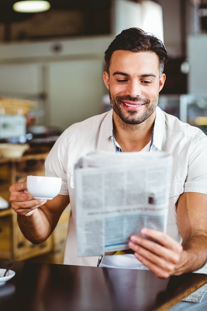 Junger Mann, der Tasse Kaffee Lesezeitung hat