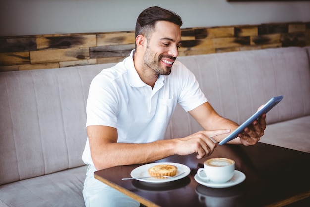 Junger Mann, der Tasse Kaffee und Gebäck isst