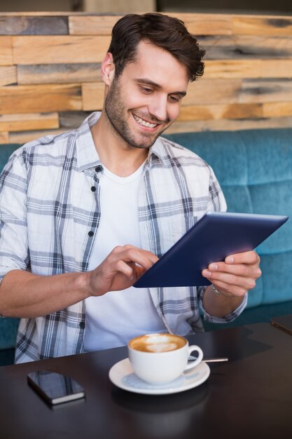 Junger Mann, der Tasse Kaffee unter Verwendung der Tablette hat