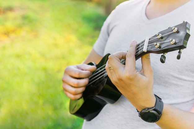 Junger Mann, der Ukulele im Park spielt