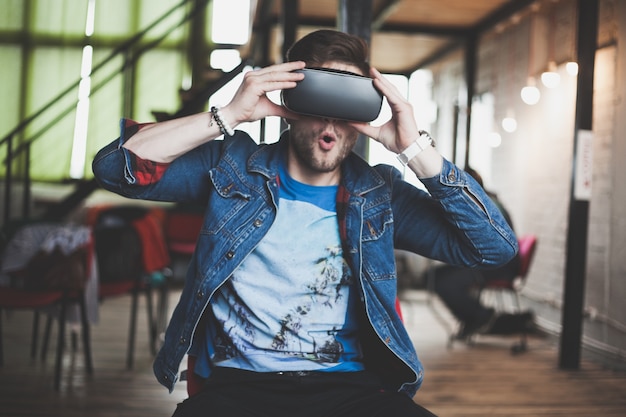 Junger Mann, der Virtual-Reality-Brille im Coworking-Studio der modernen Innenarchitektur trägt. Smartphone mit VR-Brille Headset.