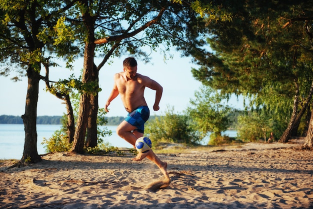 Junger Mann, der Volleyball am Strand spielt