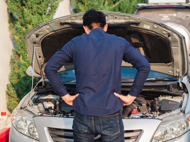 Junger Mann, der vor defektem Auto für die Prüfung des Autos steht