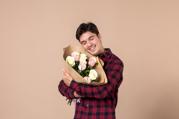 Junger Mann der Vorderansicht, der schöne Blumen auf brauner Wand hält