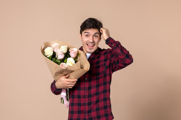 Junger Mann der Vorderansicht, der schöne Blumen auf brauner Wand hält