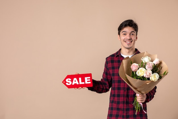 Junger Mann der Vorderansicht, der schöne Blumen und Verkaufsnamensschild an brauner Wand hält