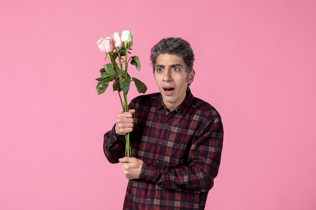 Junger Mann der Vorderansicht mit schönen rosa Rosen auf rosa Wand