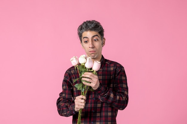 Junger Mann der Vorderansicht mit schönen rosa Rosen auf rosa Wand