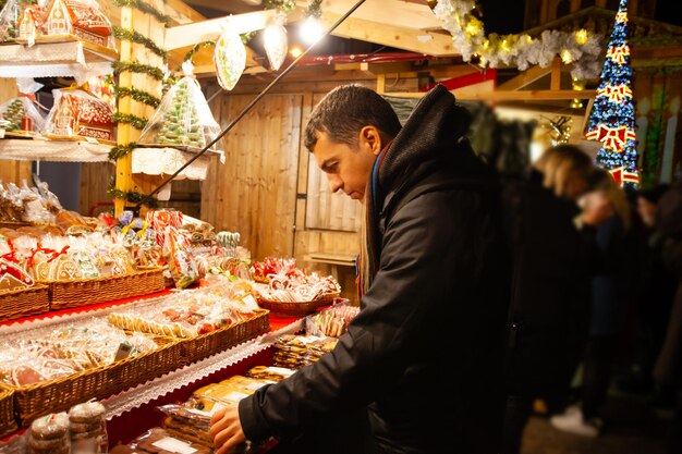 Junger Mann, der Weihnachtslebkuchen auf dem Straßenmarkt kauft Weihnachtsmarkt-Einkaufs- und Geschenkkonzept