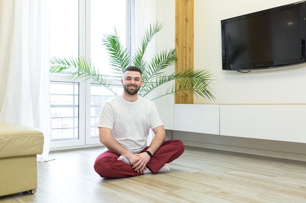 Junger Mann, der Yoga und Fitness sitzt auf dem Boden zu Hause tut