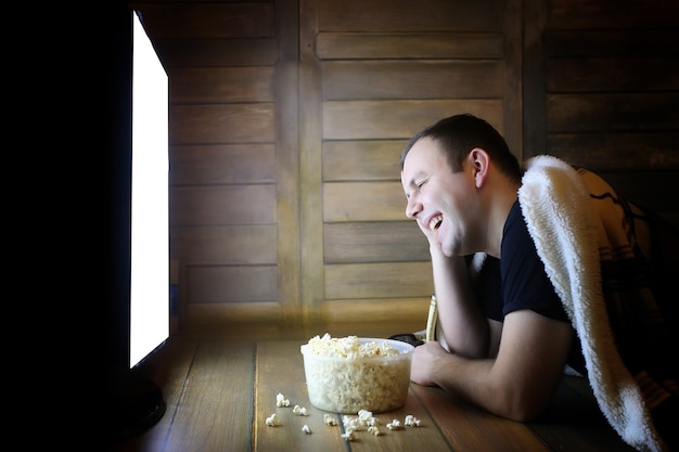 Junger Mann, der zu Hause auf dem Boden fernsieht und Popcorn isst