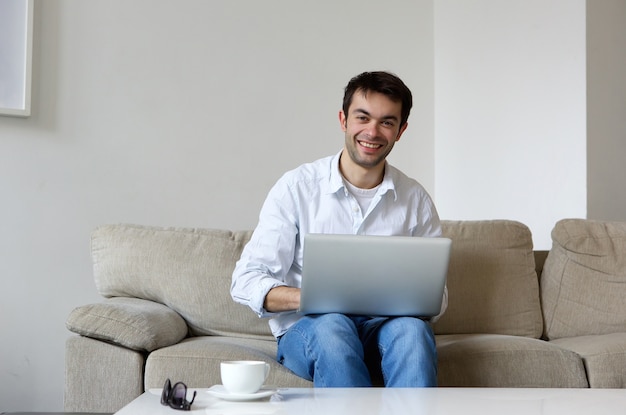 Junger Mann, der zu Hause mit Laptop lächelt