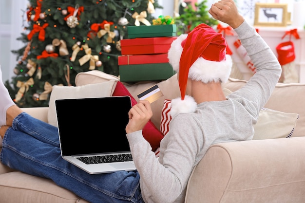 Junger mann, der zu weihnachten online mit kreditkarte zu hause einkauft