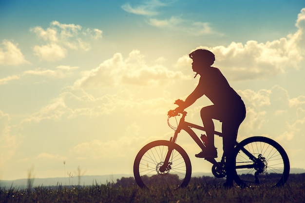 Junger Mann des Schattenbildes des Radfahrens auf Sonnenunterganghintergrund