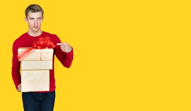 Junger Mann europäischen Aussehens auf gelbem Grund. hält Kisten mit Geschenken und zeigt mit dem Zeigefinger darauf.