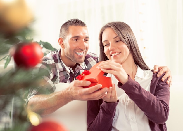 Junger Mann gibt seiner Freundin ein Weihnachtsgeschenk. Sie ist glücklich beim Öffnen der Geschenkbox.