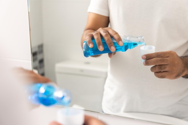 Junger Mann gurgelt mit blauem Mundwasser. Für eine gute Zahngesundheit und frischen Mundgeruch