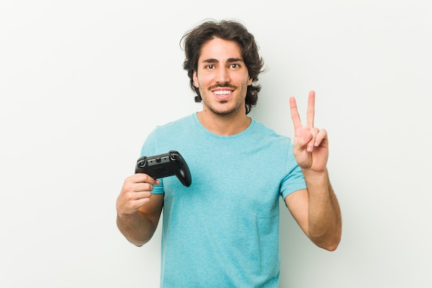 Junger Mann hält einen Gamecontroller, der Nummer zwei mit den Fingern zeigt.
