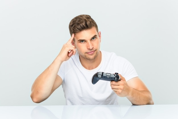 Junger Mann hält einen Gamecontroller, der seine Schläfe mit dem Finger zeigt