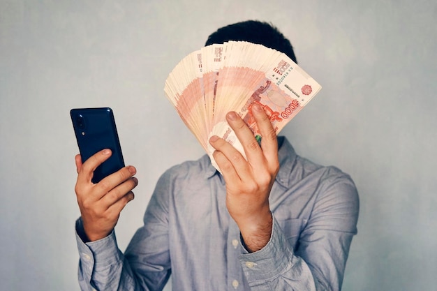 Junger Mann hält Geld in der Hand und drückt auf den Bildschirm des Smartphones Verdient Geld über die mobile App Business via Smartphone