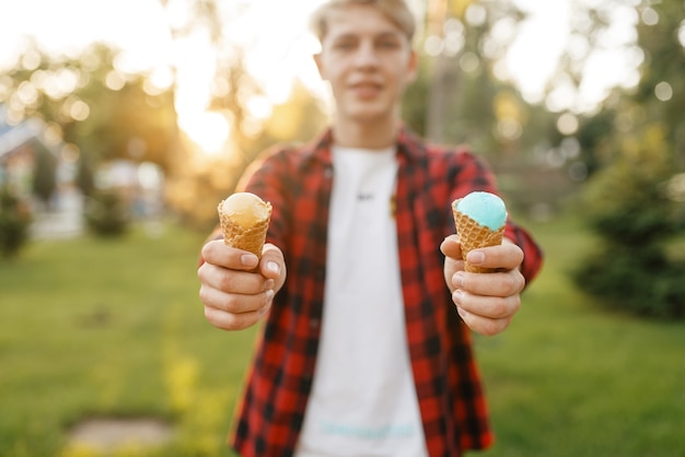Junger Mann hält im Sommerpark zwei Eiscreme in seinen Händen.
