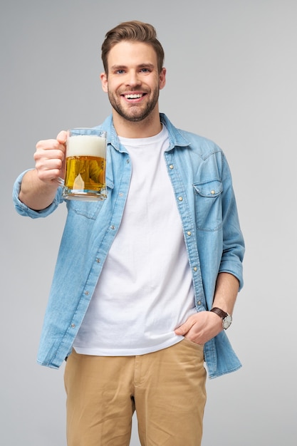 Junger Mann hält tragendes Jeanshemd, das Glas des Bieres stehend hält