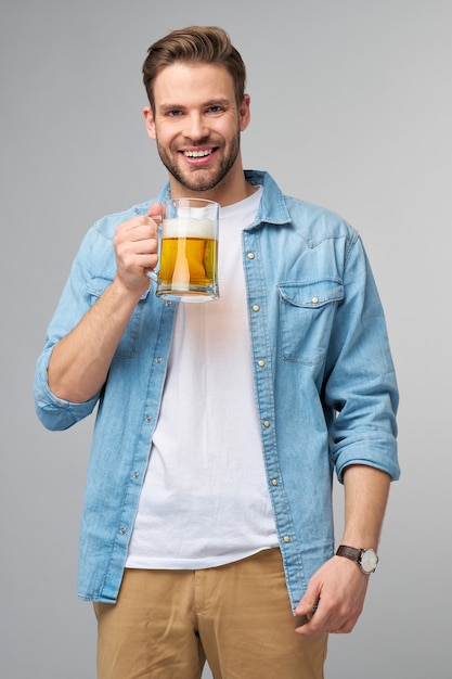 Junger Mann hält tragendes Jeanshemd, das Glas des Bieres stehend hält