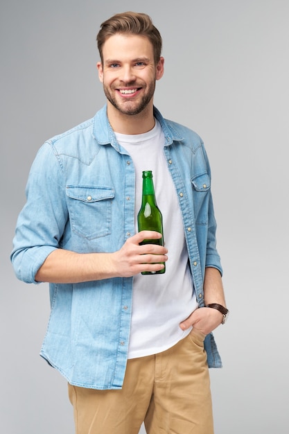 Junger Mann hält tragendes Jeanshemd Flasche Bier stehend
