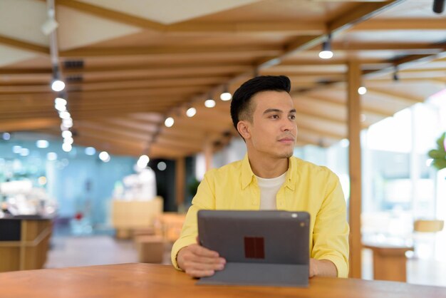 Junger Mann im Café mit digitalem Tablet-Computer beim Nachdenken