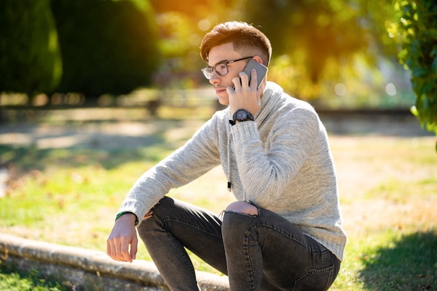 Junger Mann im grauen Pullover im Park über das Telefonieren und Kaffeetrinken. Copyspace